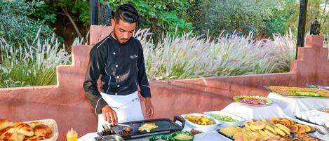 A chef preparing food outdoors with a buffet table full of various dishes.