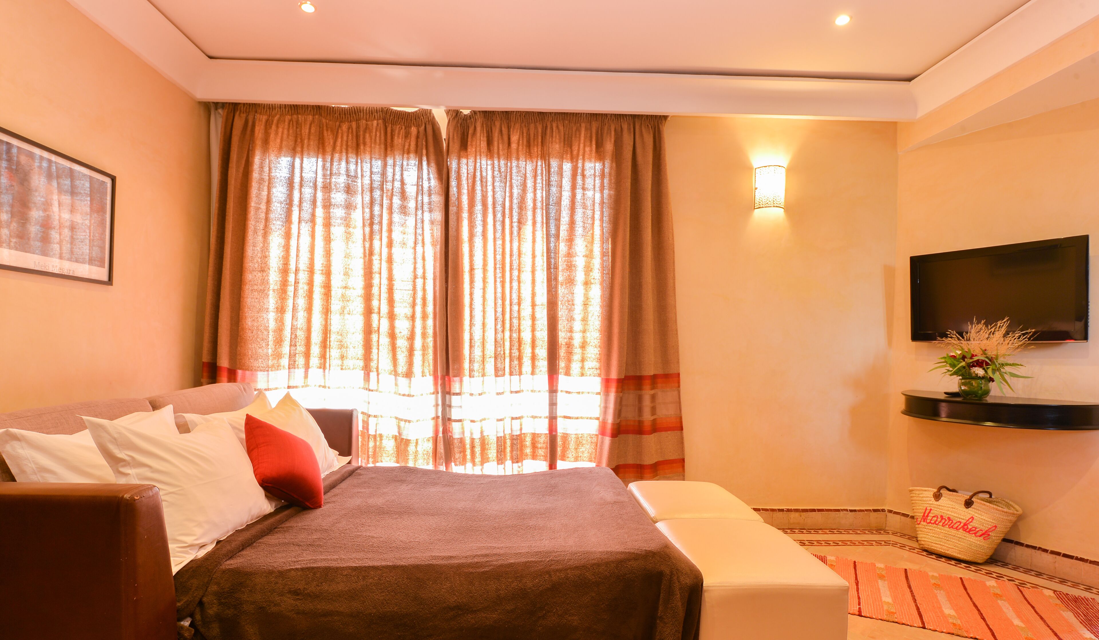 A hotel room with a bed, a sofa, a TV, and a small table with a vase.
