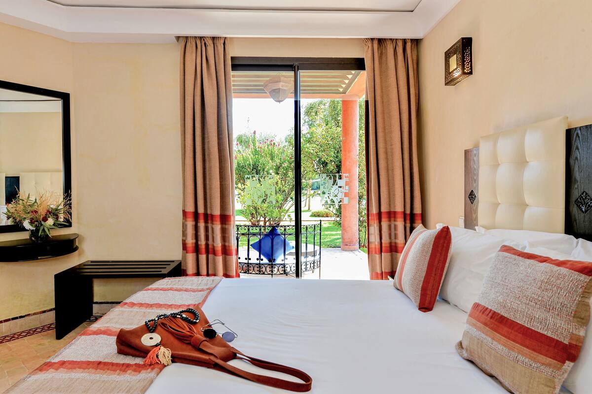 Een hotelkamer met een groot bed, een nachtkastje, een spiegel en uitzicht op een tuin door een schuifdeur.