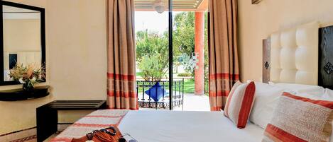 A hotel room with a large bed, a bedside table, a mirror, and a view of a garden through a sliding door.