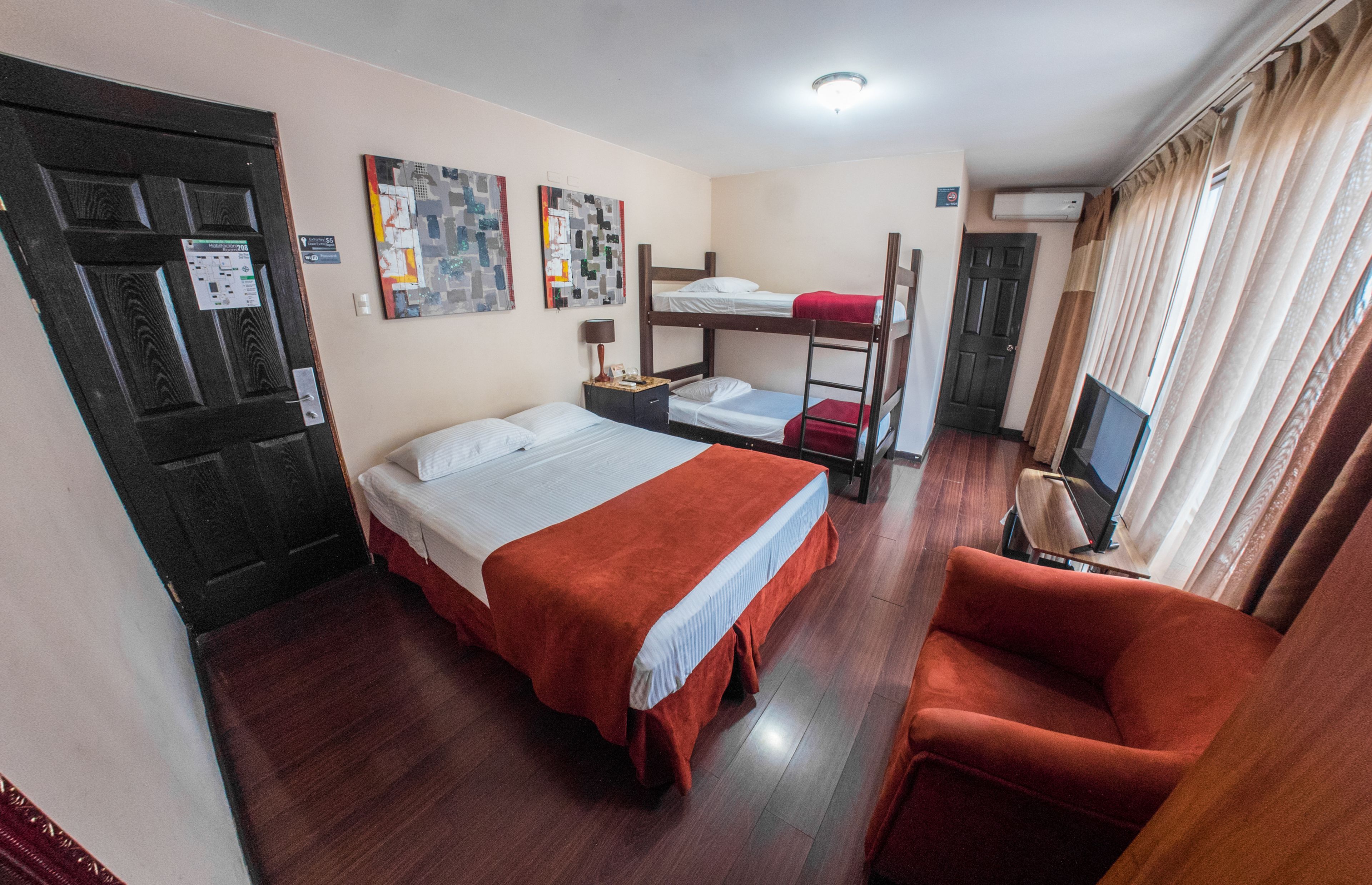 Una habitación con una cama litera, una cama individual, una silla roja, un televisor y una puerta con un letrero.