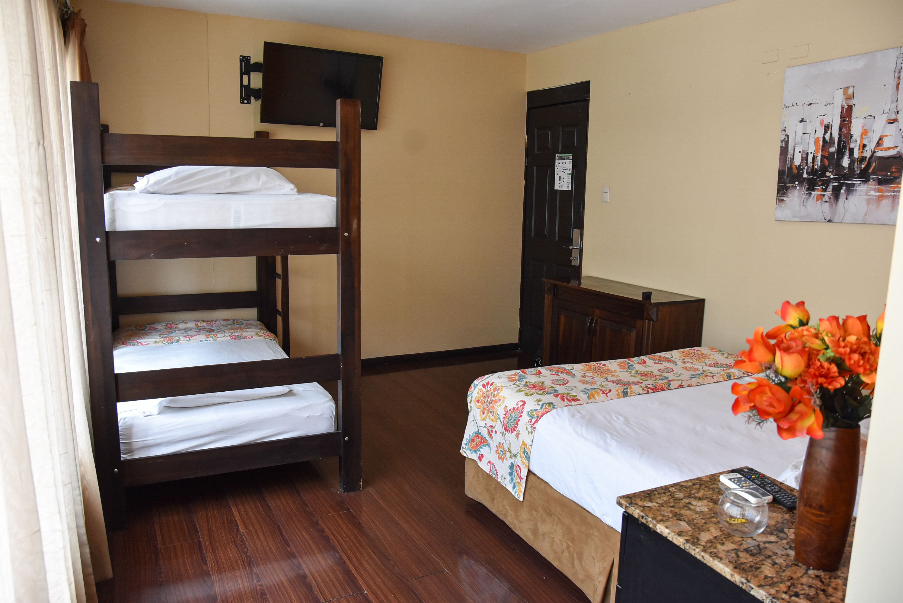 A room with a bunk bed, a desk, a chair, a vase with flowers, and a painting on the wall.