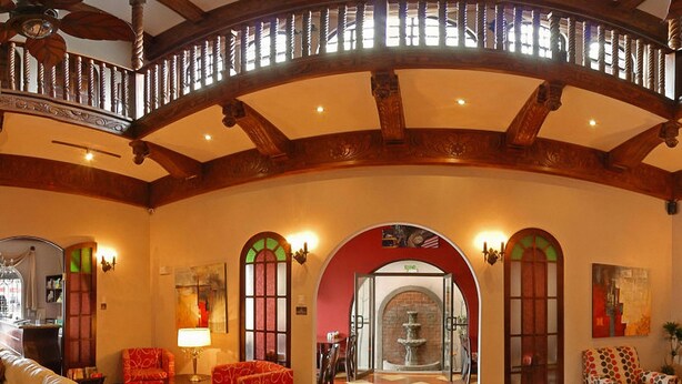 Un amplio salón con sofá rojo, suelo de madera y techo alto con vigas a la vista.