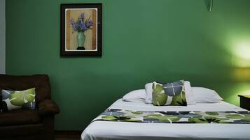 A room with a bed, a chair, a nightstand with a lamp, and a framed picture on the wall.