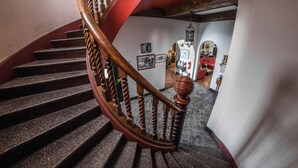 Una escalera de caracol con balaustradas de madera y barandilla roja, que conduce a una habitación con cuadros enmarcados y un sillón rojo.