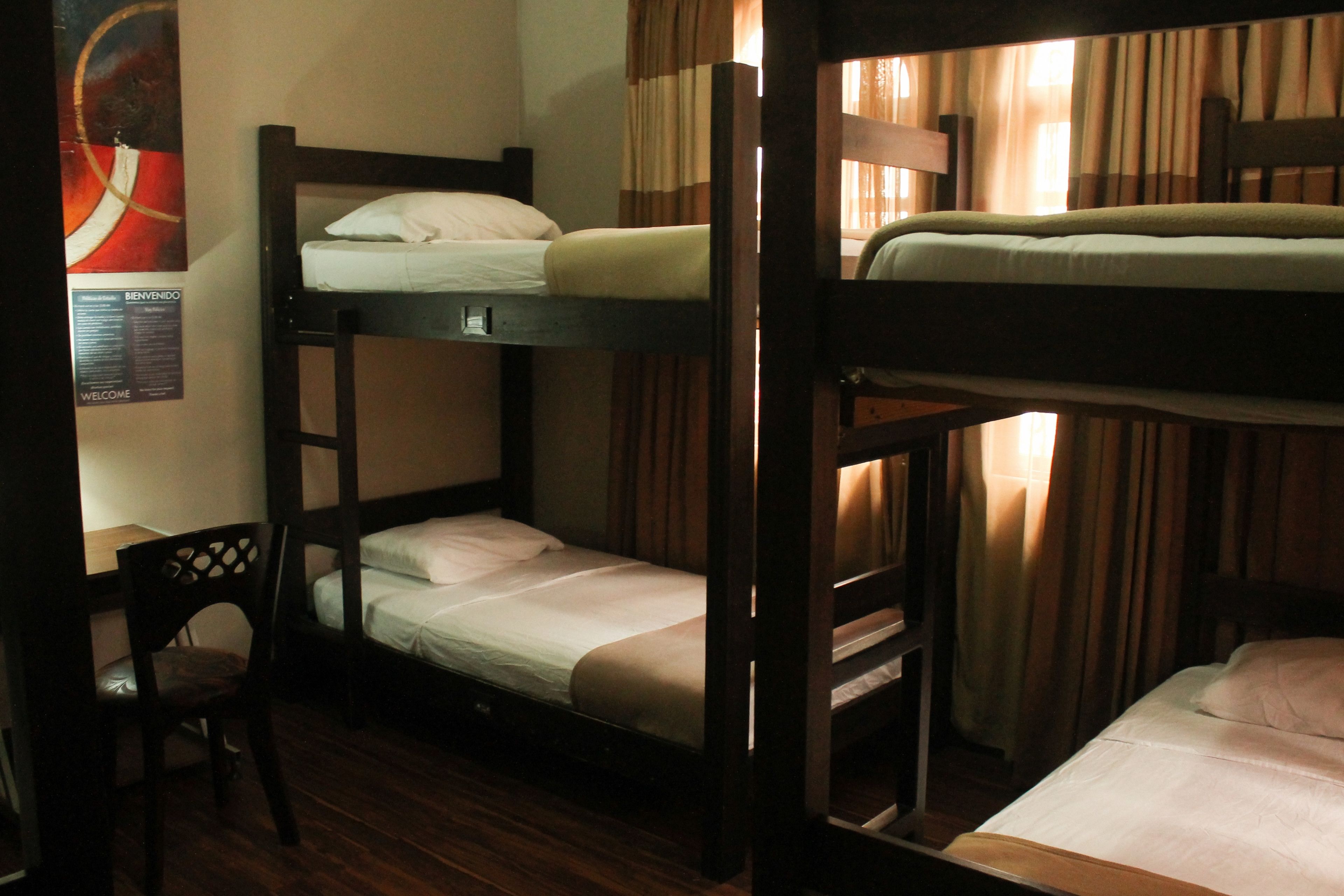 A bunk bed room with wooden frames, a small desk, and a chair.