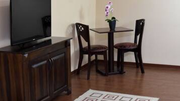 A room with a wooden cabinet, a flat-screen TV, two chairs, a small table, and a potted orchid.