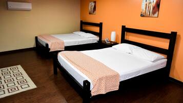 A hotel room with two single beds, a wooden floor, a patterned rug, and artwork on the walls.