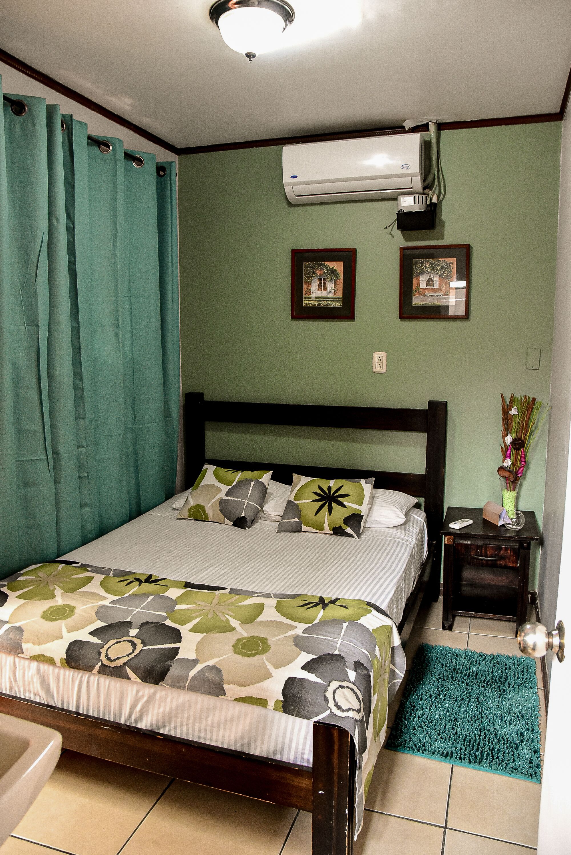 A bedroom with a bed, a nightstand, an air conditioner, and a bathroom.