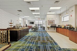 Un amplio vestíbulo de hotel con alfombra estampada, un mostrador de recepción y un área de comedor.