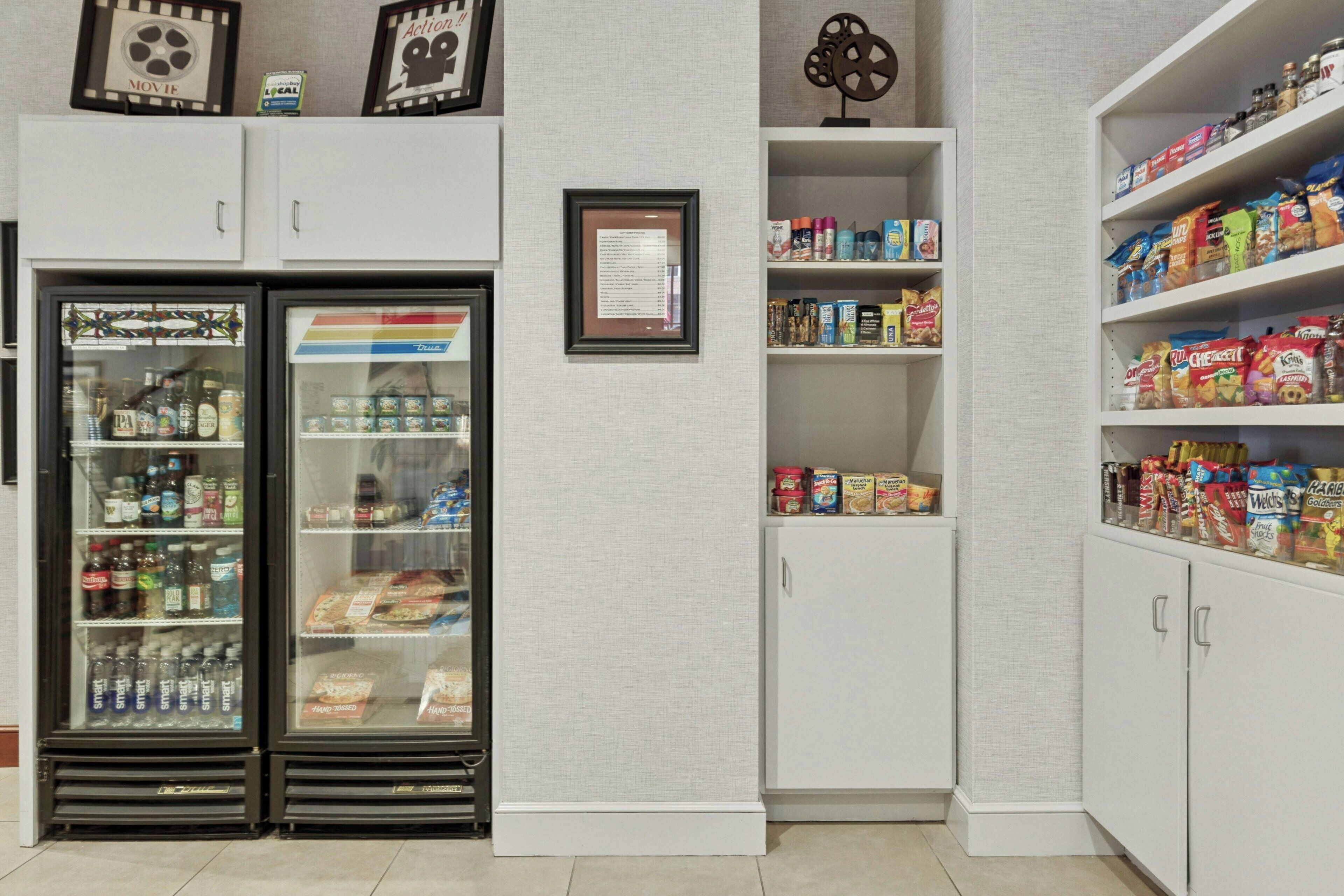 A kitchenette with a refrigerator, pantry, and shelves stocked with snacks and beverages.