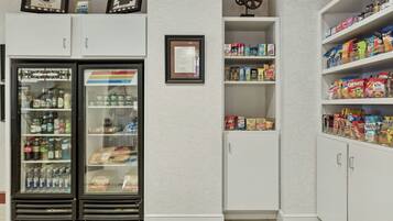 A kitchenette with a refrigerator, pantry, and shelves stocked with snacks and beverages.