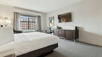 Habitación de hotel con una cama grande, un escritorio, una silla, un televisor y una ventana con vistas a la ciudad.