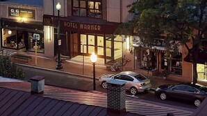 Un hotel con un llamativo letrero 'Hotel Warner', una fachada moderna y una entrada a nivel de calle con autos estacionados frente a él.