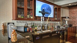 Zona de bar con un televisor mostrando un anuncio de cerveza, una variedad de botellas y un grifo de cerveza con forma de perilla.