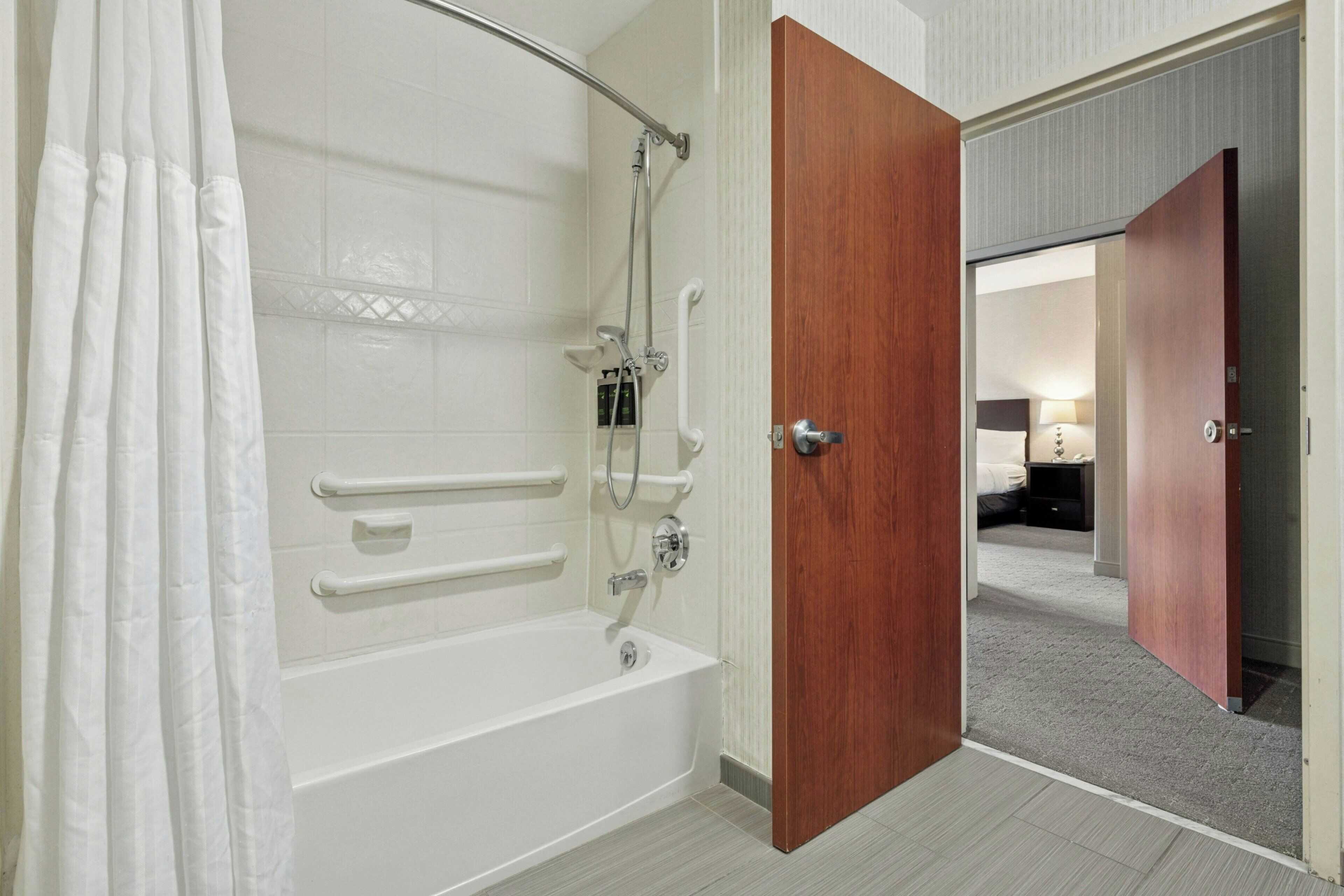 A bathroom with a bathtub, shower, and grab bars.