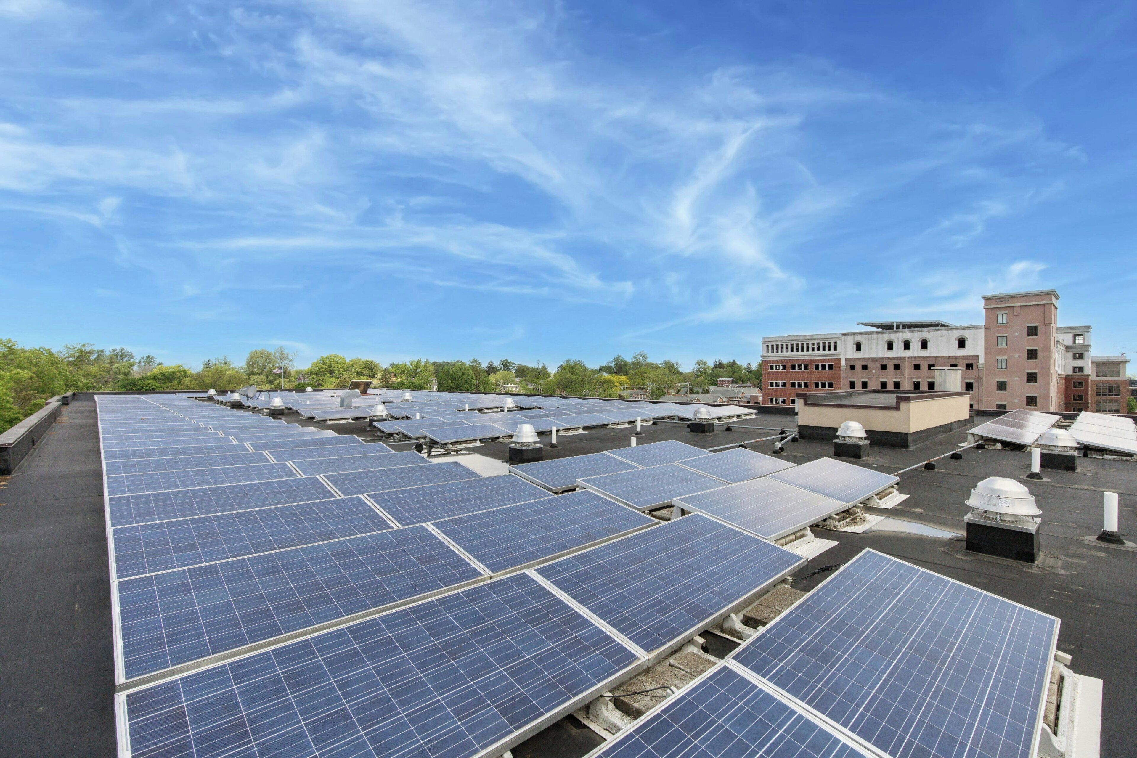 Una azotea con varias filas de paneles solares y un edificio de techo plano al fondo.