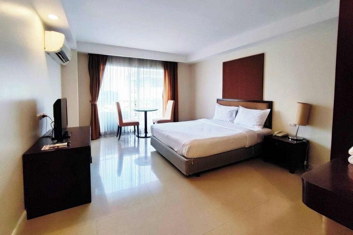 Een hotelkamer met een bed, nachtkastje, lamp, stoel en een bureau met een computer.