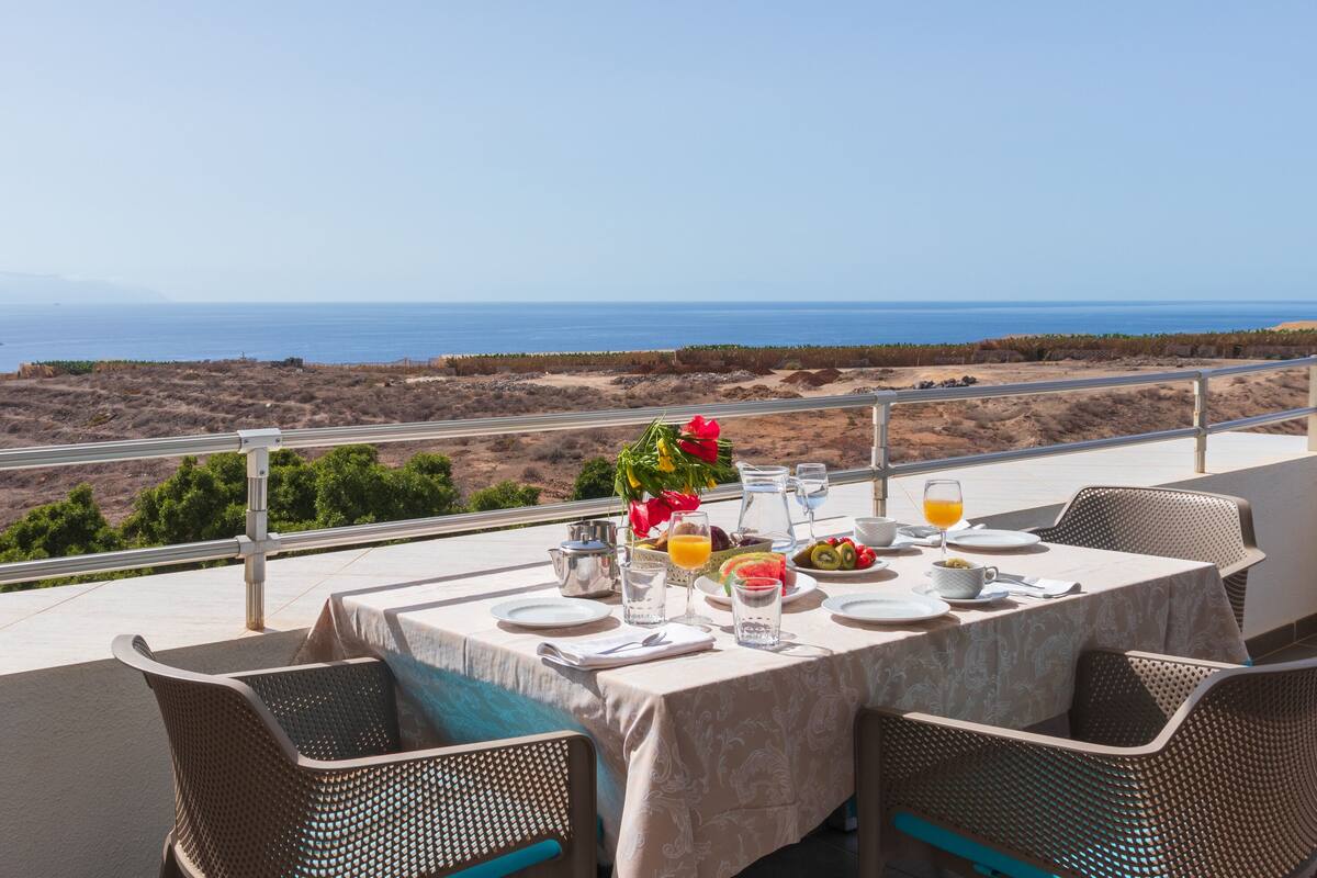 A table set for dining with a view of the ocean and hills.