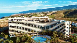 A multi-story hotel with a pool surrounded by palm trees and a view of the ocean and mountains. - Club Hotel Marazul (Adeje)