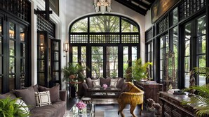 A spacious living room with a large arched window, a sofa set, a coffee table, and various decorative items including a tiger statue and books. - The Siam (Bangkok)
