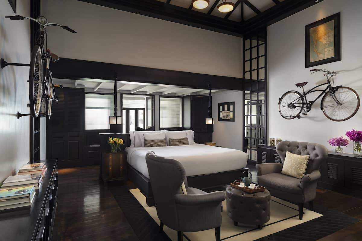 Un dormitorio moderno con una cama grande, una bicicleta colgada en la pared y una zona de estar con un sillón y reposapiés.