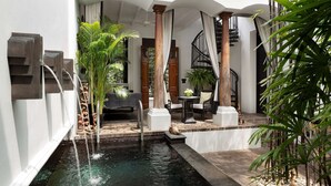 A serene indoor garden with a central water feature, stone steps, and a seating area with a table and chairs. - The Siam (Bangkok)