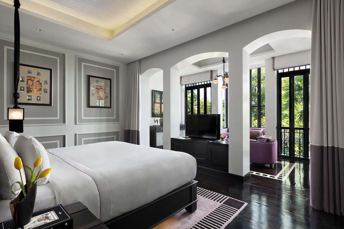 Un dormitorio moderno con una cama grande, televisión y vistas a zonas verdes por las ventanas.