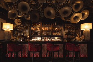 A bar with multiple hanging brass instruments, a well-stocked liquor shelf, and red upholstered bar stools.