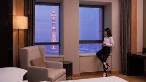 Hotelkamer met een groot raam dat uitzicht biedt op een toren, een bed, een stoel en een bureau.