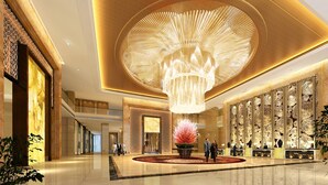 Een ruime lobby met een grote kroonluchter, een receptiebalie en een decoratieve wand met ingewikkelde patronen.