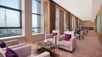 A hotel room with a large window, striped sofas, a marble coffee table, and a dining area with chairs and a table.