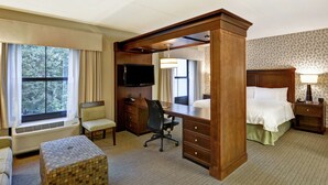 Une chambre d’hôtel avec un grand lit, un bureau avec une chaise, une télévision, une lampe et une fenêtre avec des rideaux.