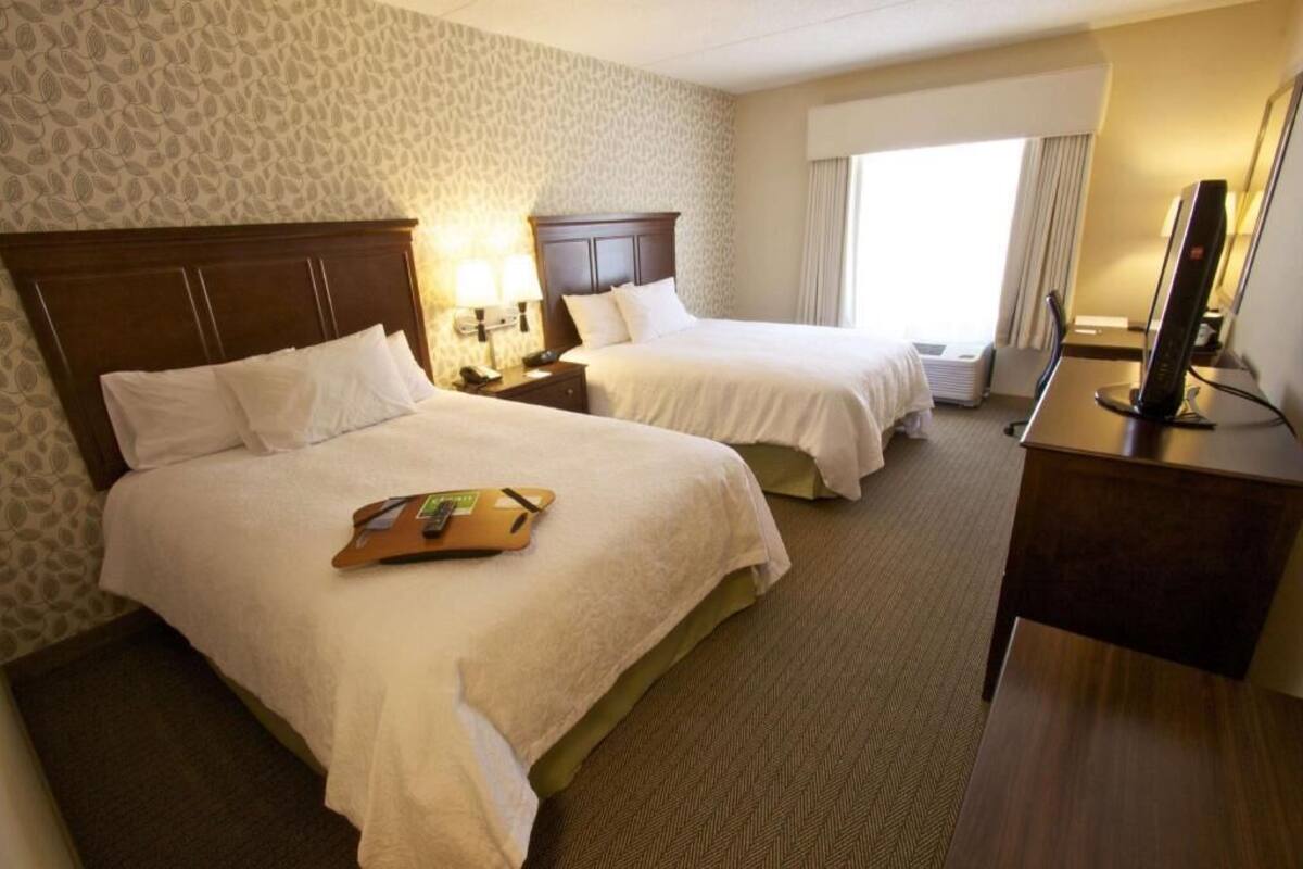 Habitació d'hotel amb dos llits, un escriptori, un televisor i una finestra amb cortines.