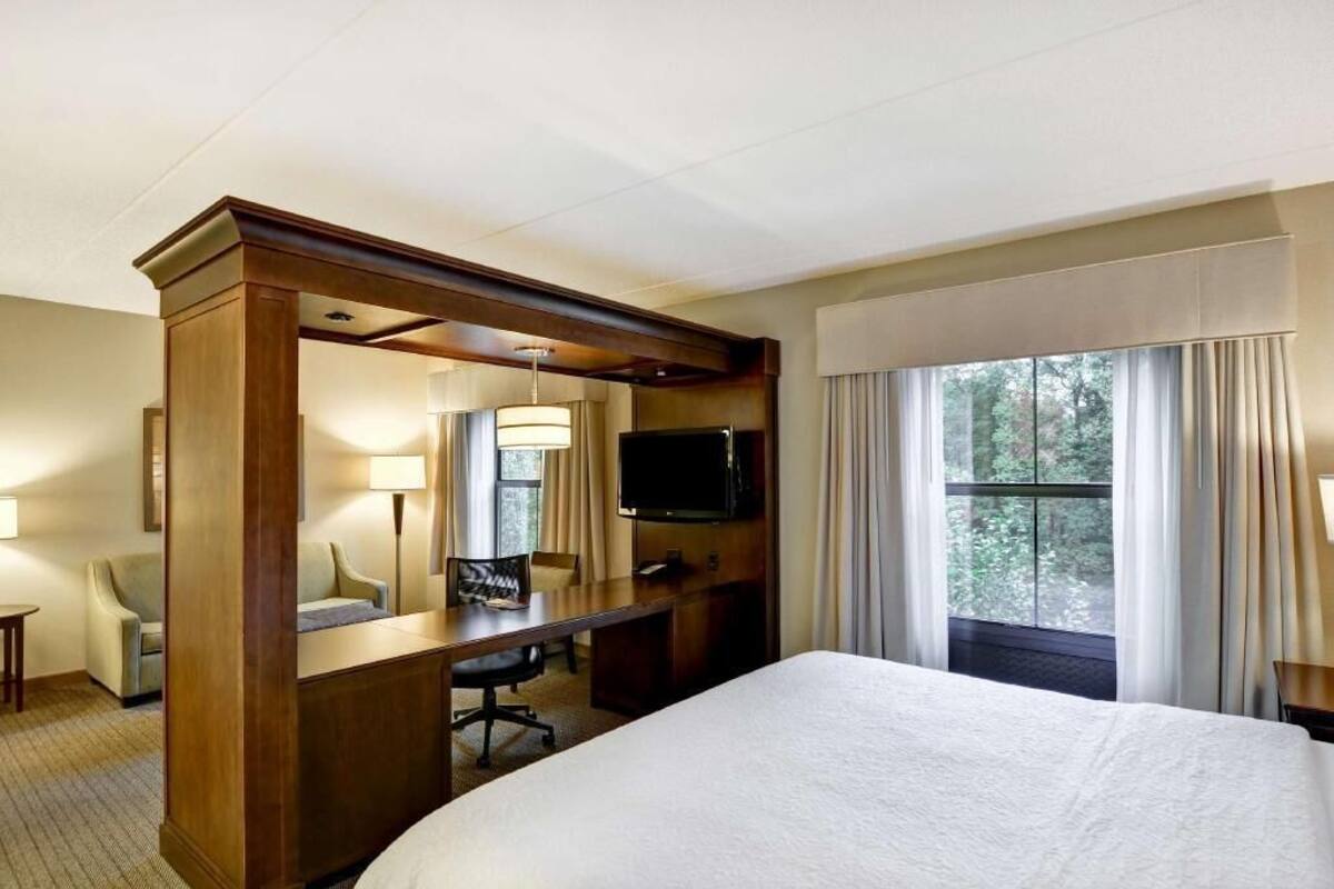 Una habitació d'hotel amb un llit, escriptori, cadira, televisió i finestra amb cortines.
