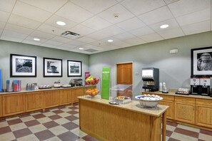 A self-service breakfast area with a checkered floor, wooden cabinets, a coffee machine, and various food items.