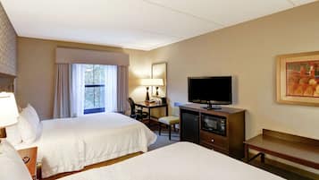 A hotel room with two beds, a desk with a lamp, a television, and a painting on the wall.
