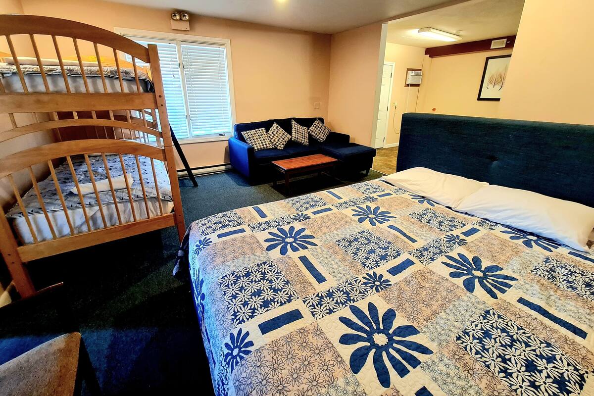 A bedroom with a bunk bed, a sofa, and a bed with a patterned quilt.