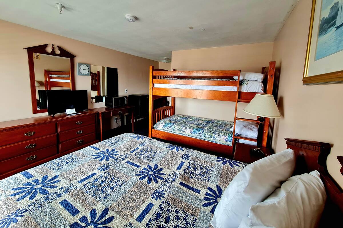 A hotel room with a bunk bed, a desk with a computer, a dresser, a mirror, and a painting on the wall.