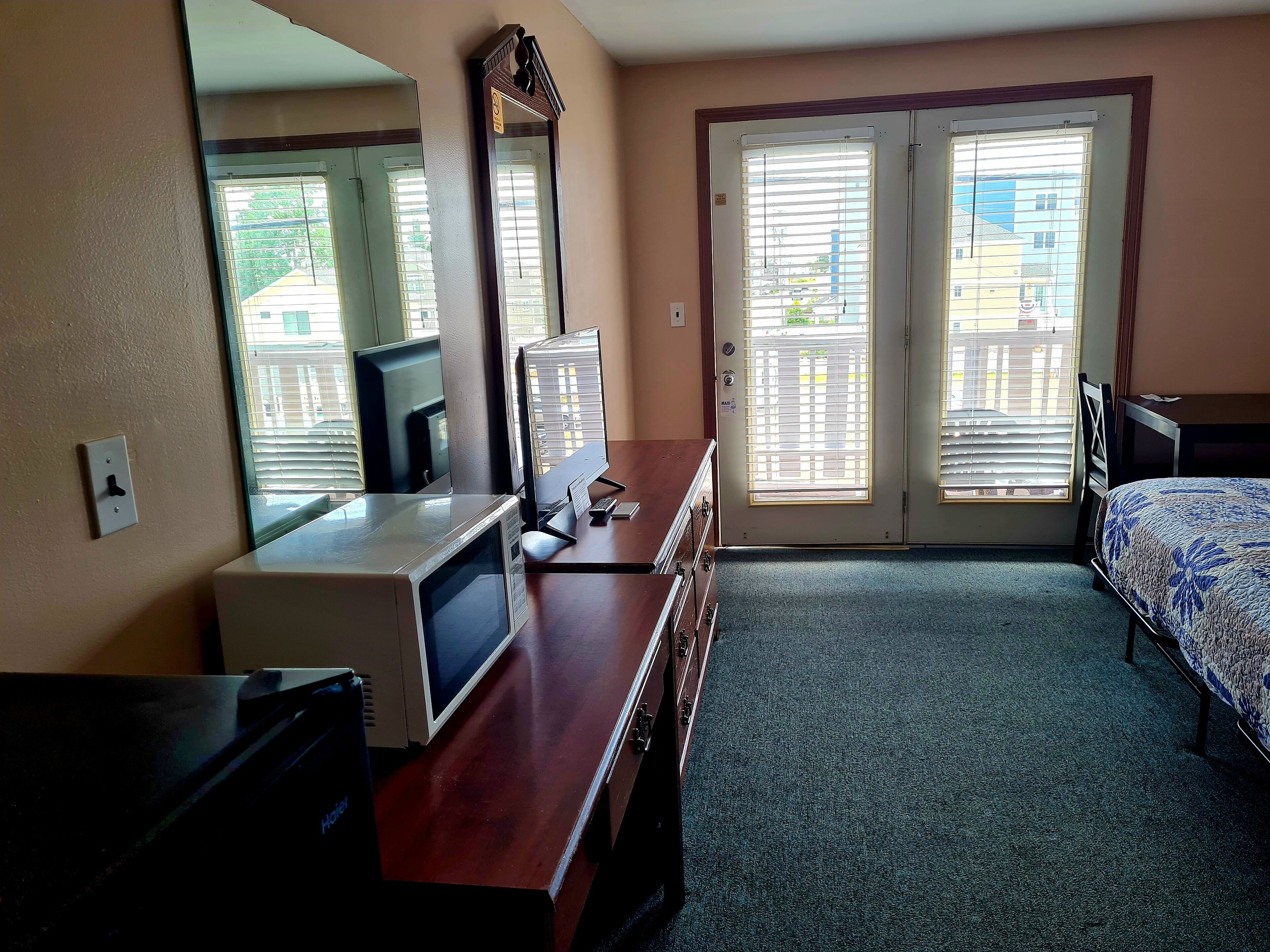 A hotel room with a desk, a mirror, a bed, and a view through the door.