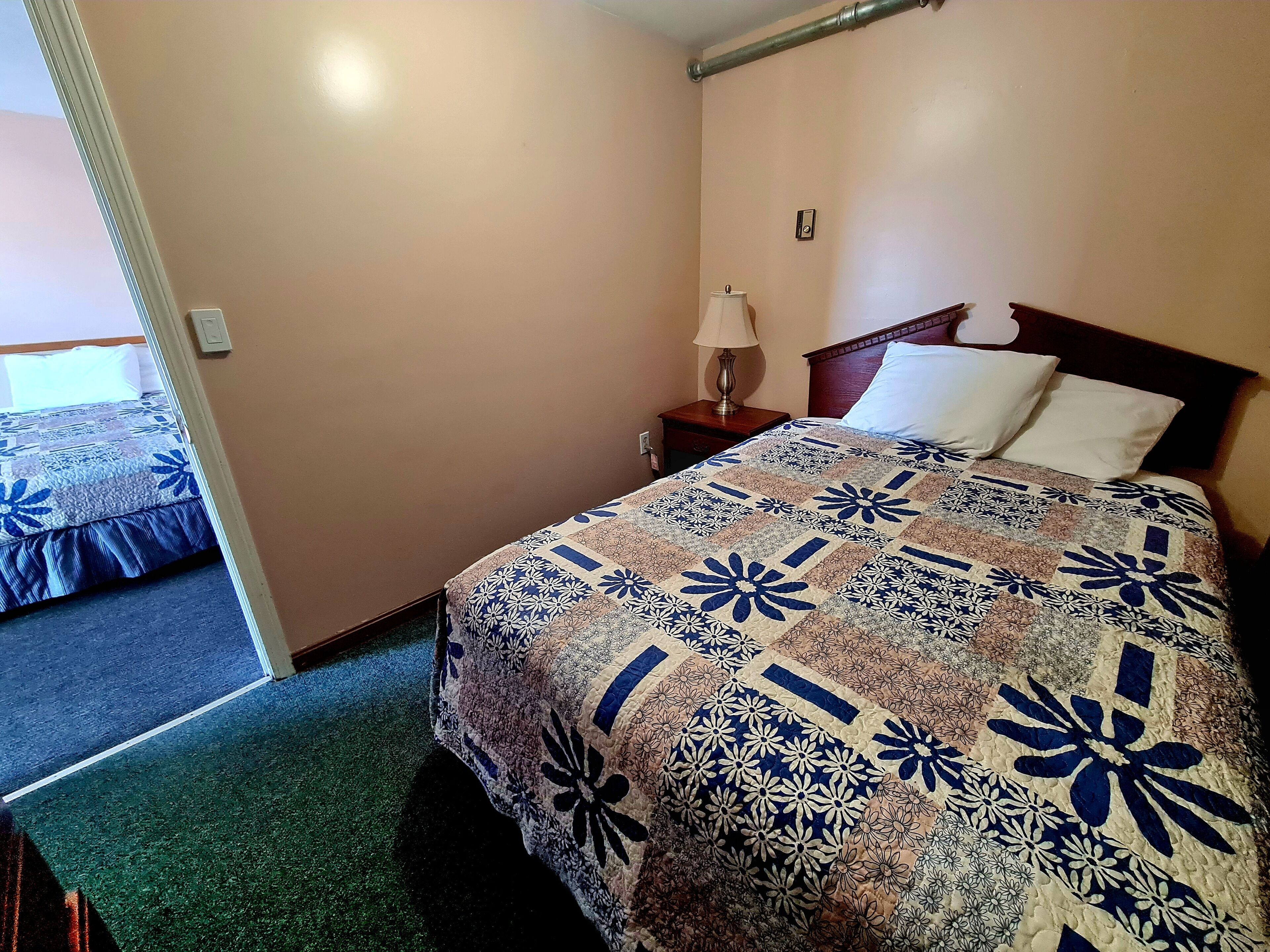 Ett hotellrum med en säng, ett nattduksbord, en lampa och en dörr.
