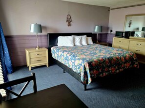 A neatly arranged hotel room with a bed, two bedside tables with lamps, a dresser, and a wall-mounted dreamcatcher. - Regal Inn (Hampton)