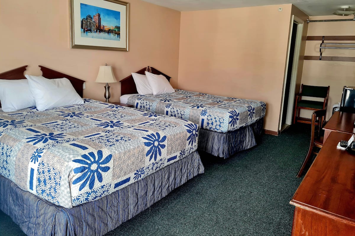 A hotel room with two beds, a desk, a chair, a lamp, and a painting on the wall.