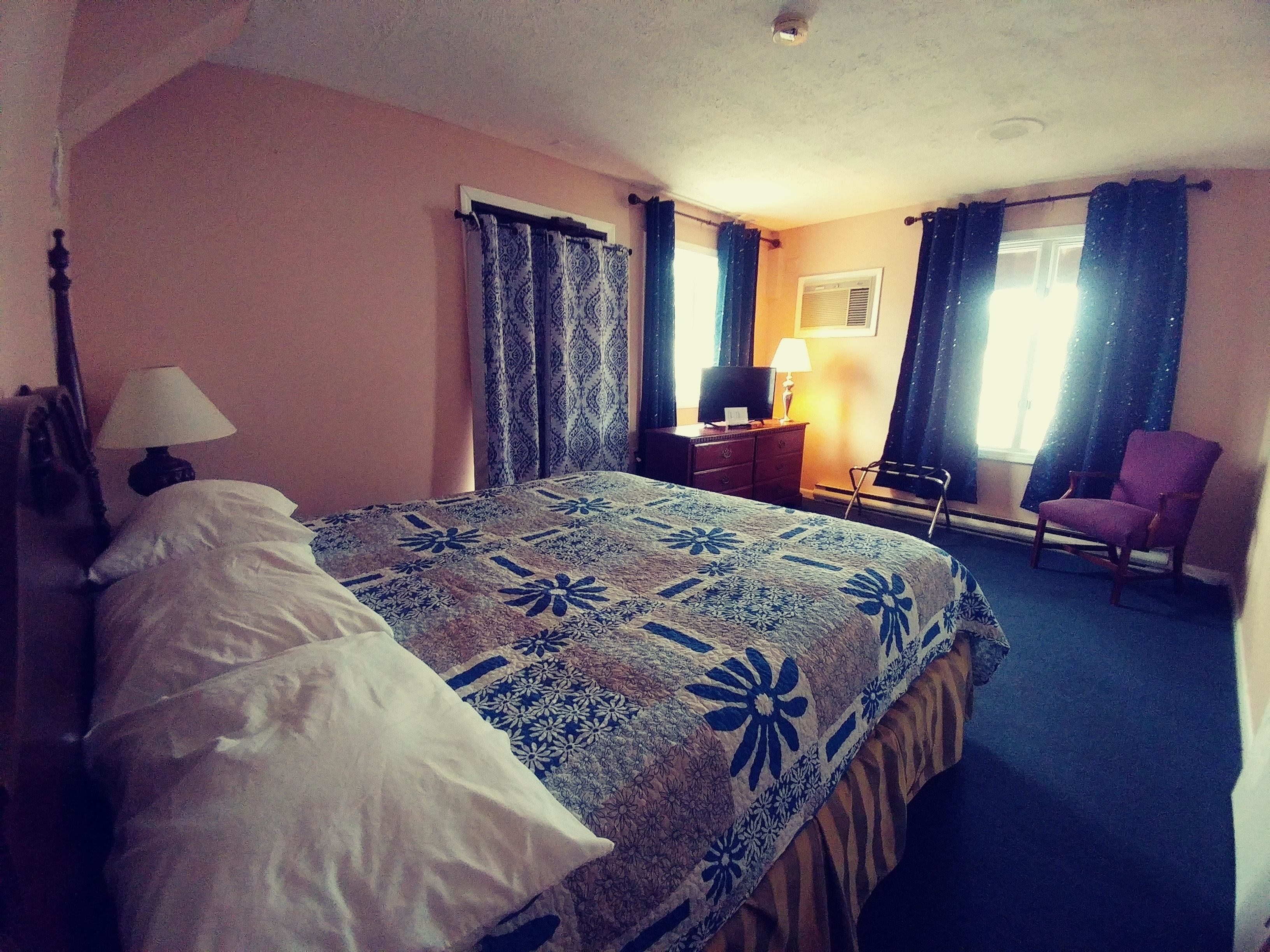 A hotel room with a bed, a desk, a chair, and a window with curtains.