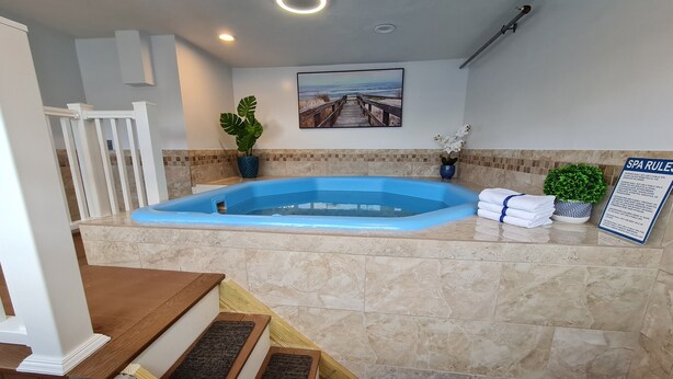 A spa area with a blue hot tub, a wooden bench, a potted plant, and a sign with spa rules. - Regal Inn (Hampton)