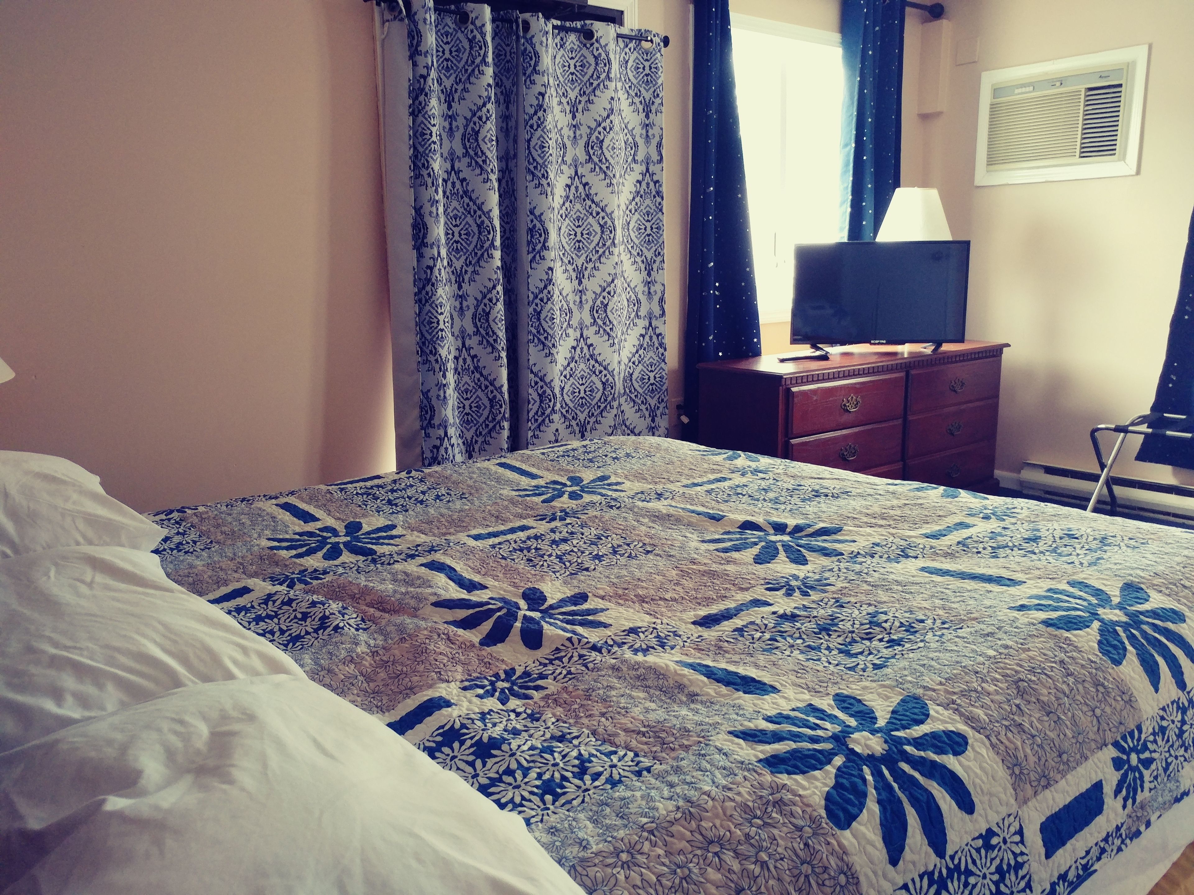Een slaapkamer met een bed, een dressoir, een televisie en een raam met gordijnen.