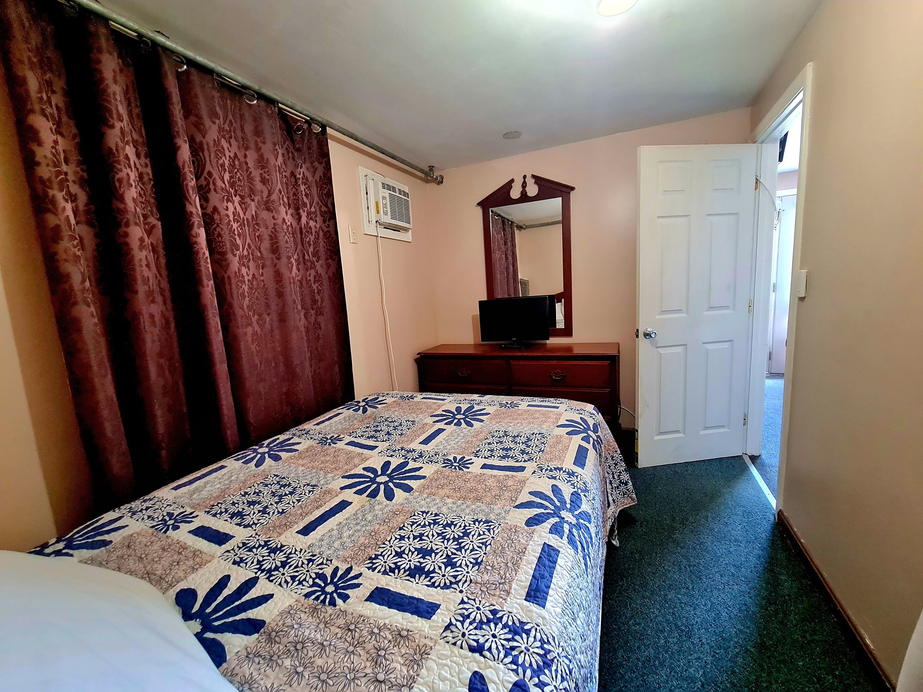 A bedroom with a bed, a dresser, a mirror, and a door.