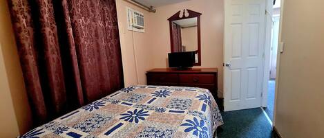 A bedroom with a bed, a dresser, a mirror, and a door.