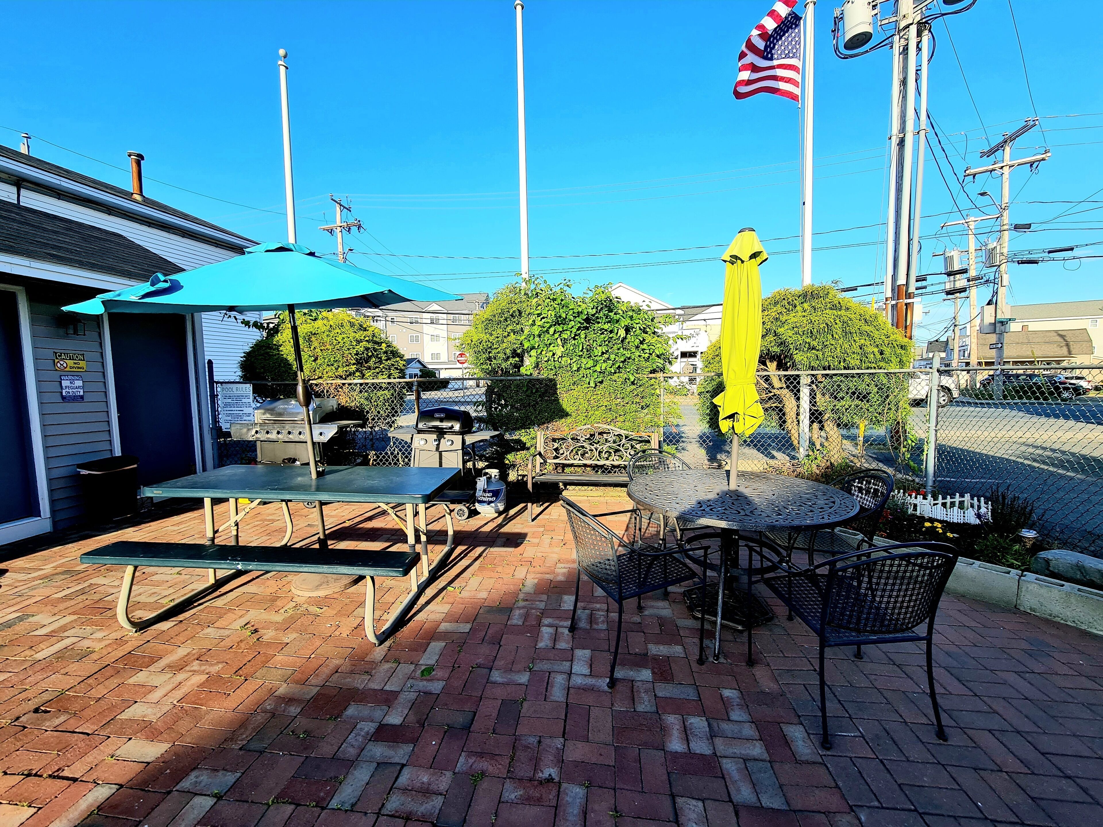 An outdoor patio with a grill, tables, and chairs, a yellow umbrella, and an American flag.