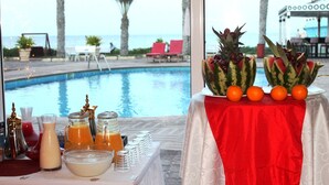 Mesa junto a la piscina con bebidas y frutas, con vista a la piscina y la playa.